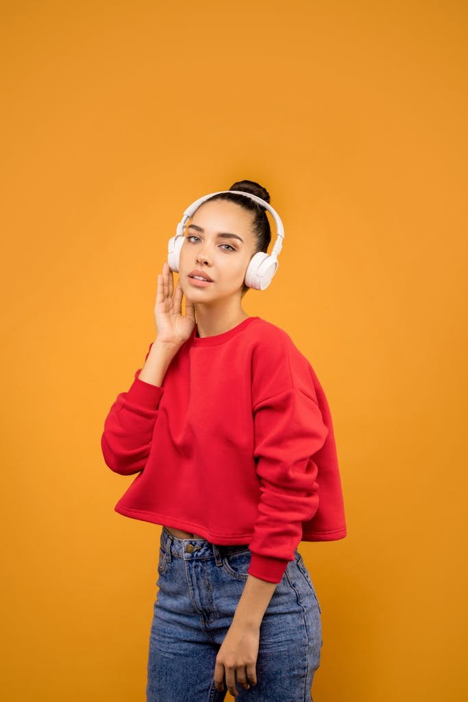 Stylish young adult woman enjoying music with headphones, wearing red sweater and jeans.